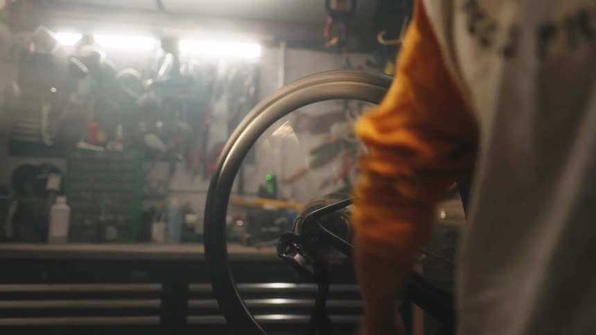 A woman turning the crank and pedals of a bicycle inside a workshop causing the wheel to spin