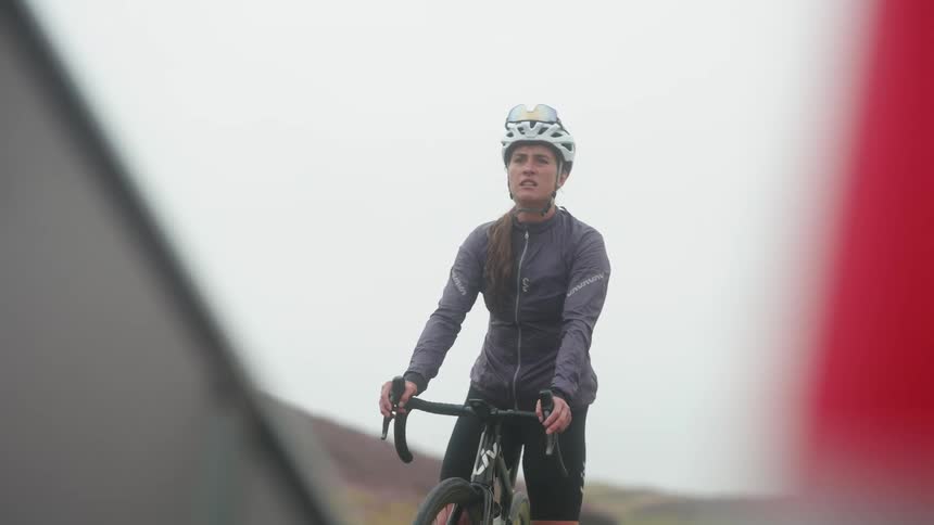 Female cyclist stops on a paved path to look past a barrier