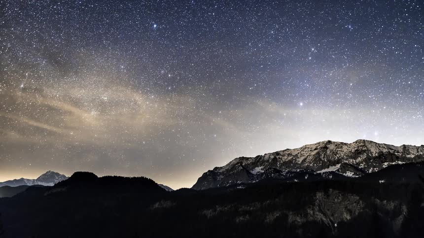 A starry night with a bright sky passing quickly in a place with mountains