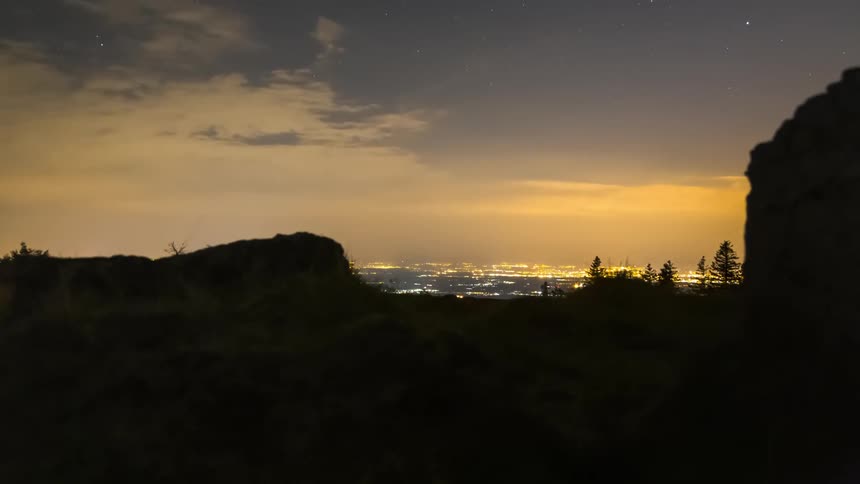 Silhouette of rocks and an illuminated city in the background at dusk