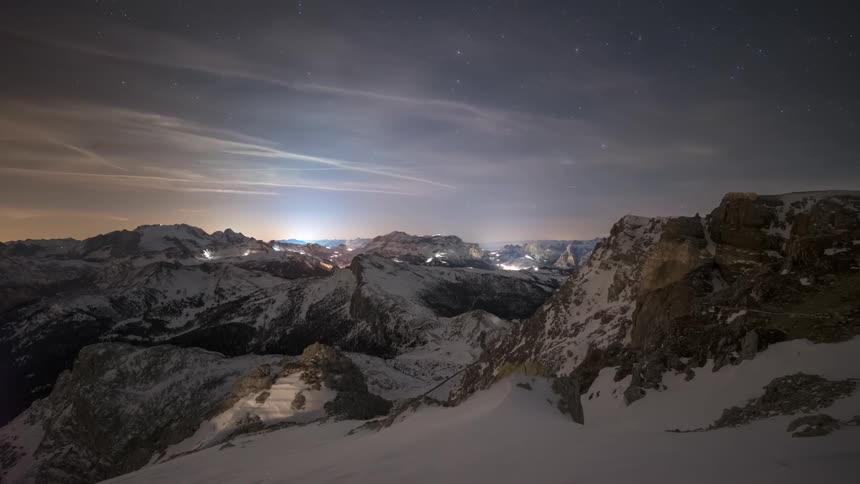 A snowy mountain landscape at night cars driving through illuminated by starlight
