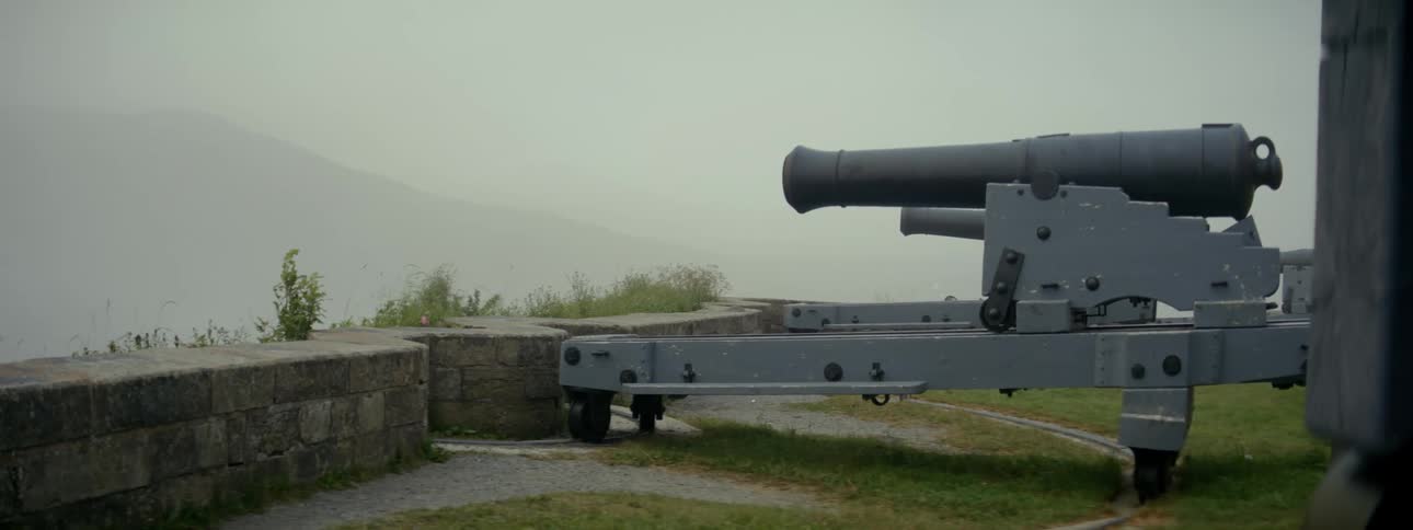 An old gray cannon on a metal base with wheels next to an incline
