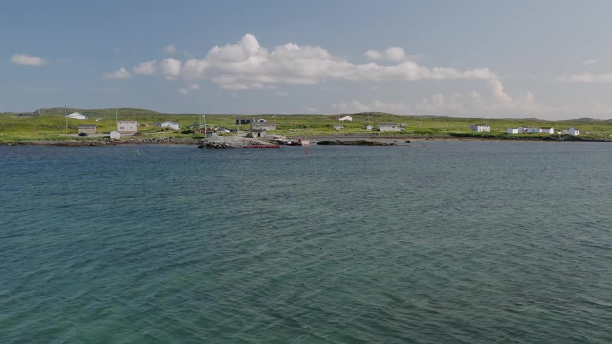 Aerial view of a seaside village with docked boats and rolling green fields