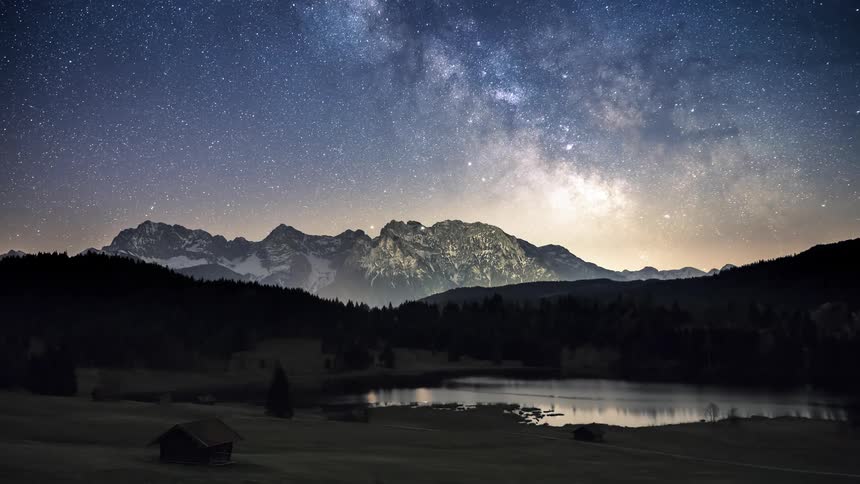 Night landscape with a starry sky above snowcapped mountains a peaceful lake in the foreground and the dawning day