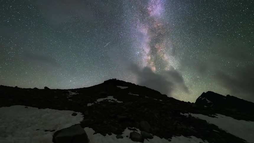 A time lapse shows clouds pass over mountains beneath a starry night sky