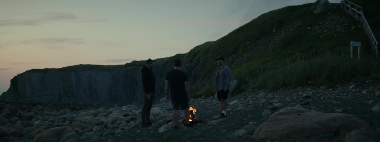 Men gathered around a campfire with a cliff in the background