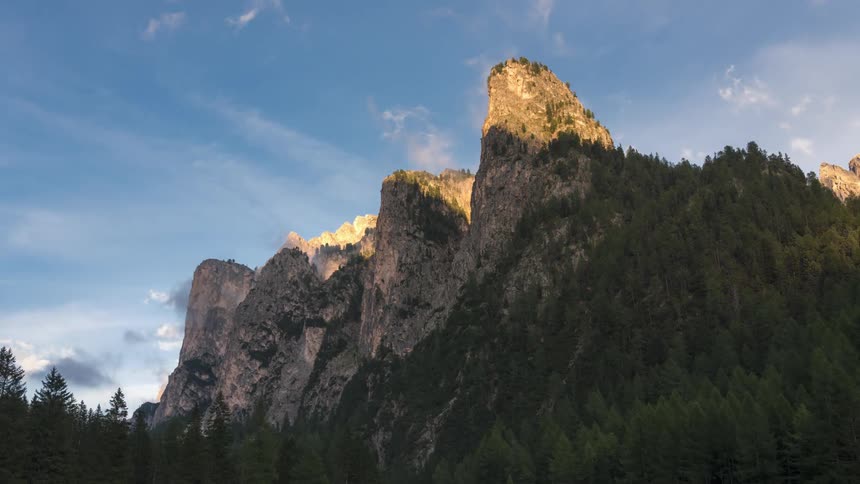 Time lapse of sunset shadows moving over the mountains under a blue cloudy sky