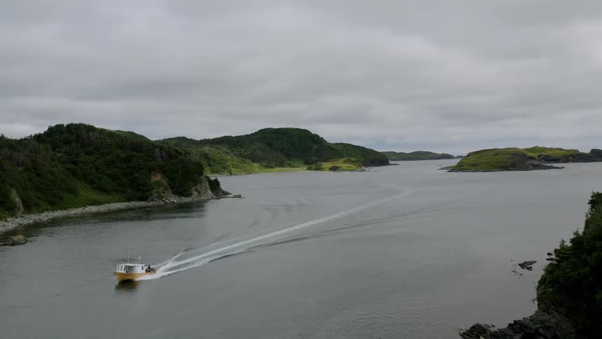 Boat sailing through a sea channel surrounded by rugged wooded terrain under a cloudy sky