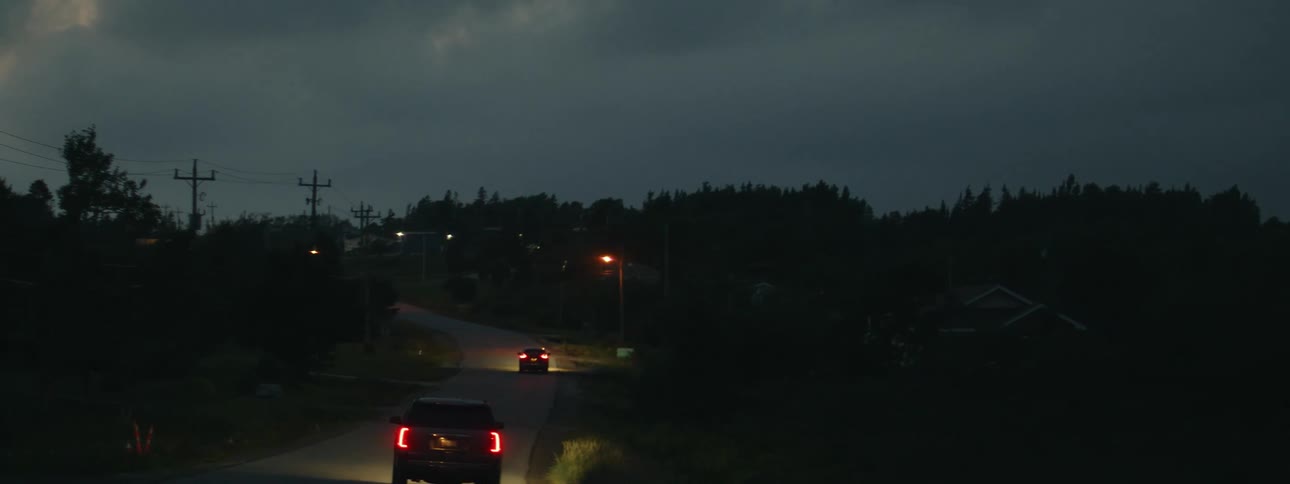 Two cars are driving down a rural road at night