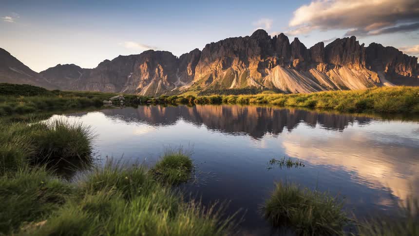 Lake waters reflect clouds passing toward mountains