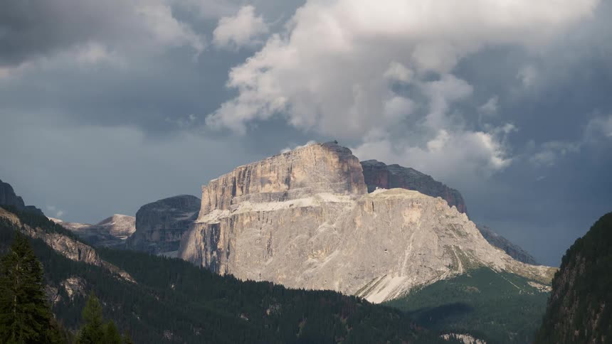Clouds through overcast sky casting shadows onto forested slopes of mountains