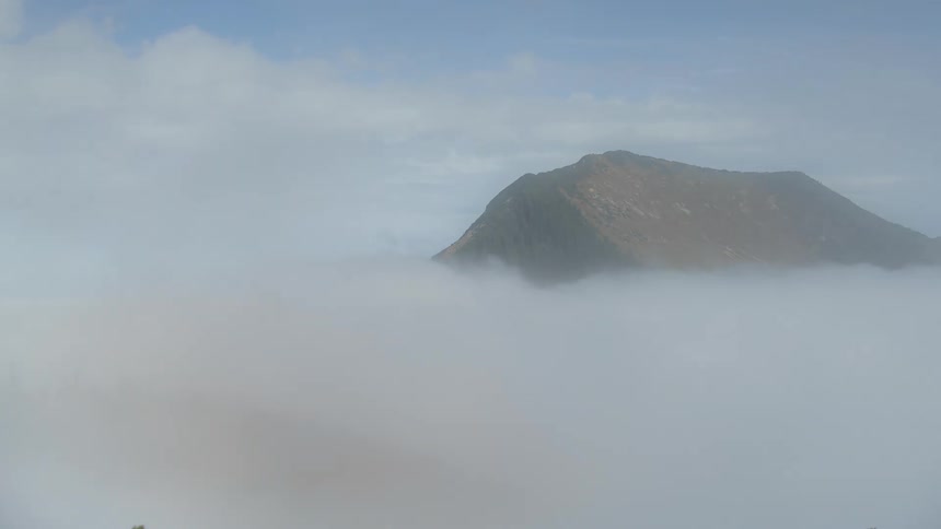 Flowing low lying clouds obscure forested mountains