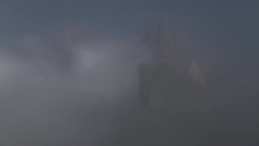 A stone mountain with a cloud passing over it and then everything becomes foggy