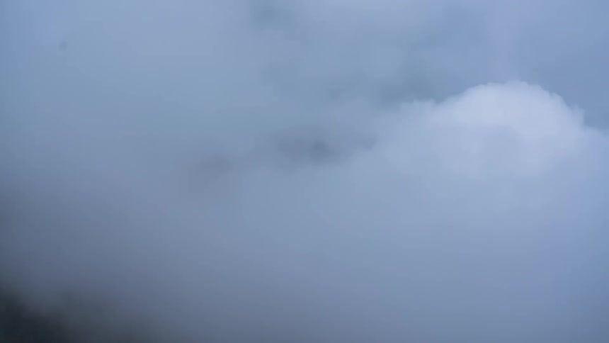 A dense white cloud moving through the mountainous environment