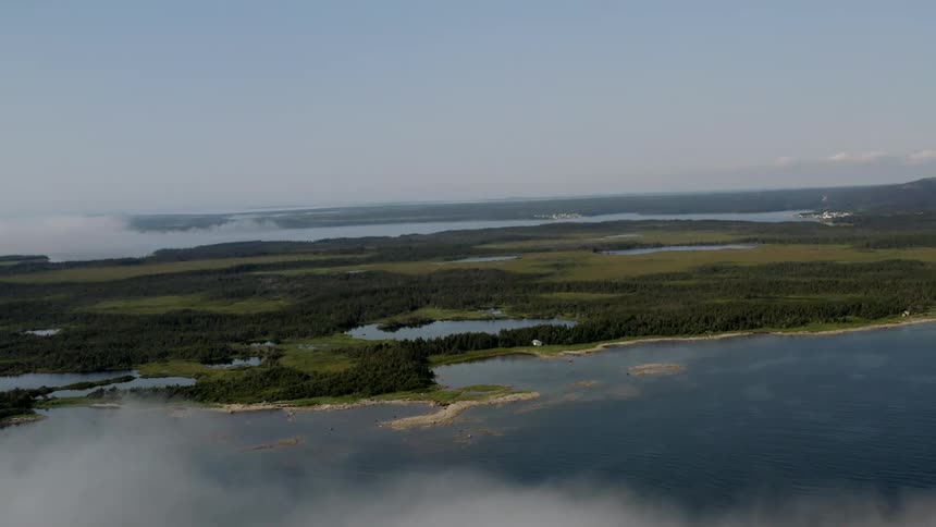 Aerial view of a landscape with patches of water bodies surrounded by dense vegetation partially obscured by lowlying clouds or fog