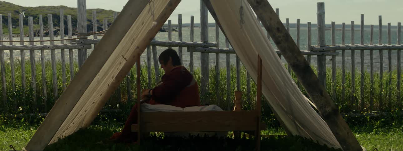 Woman sits under aframe tent separated by fence from coast on a breezy day