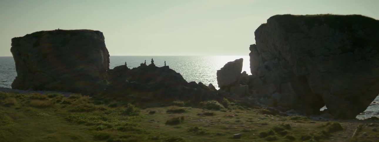 Some large stones on the sand of a beach and behind them there is the horizon with the ocean