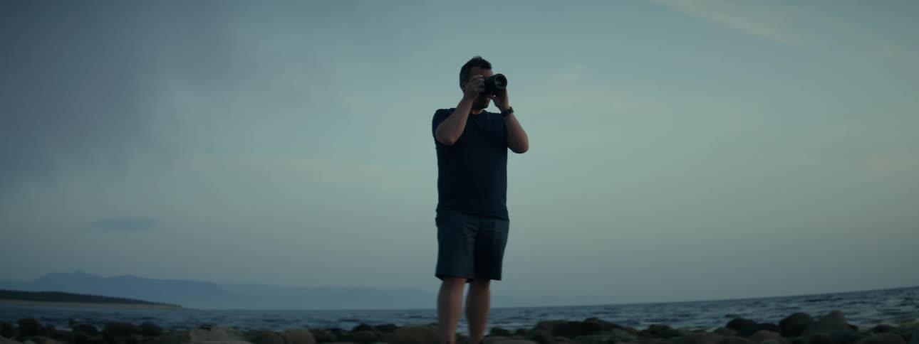 Man on top of rocks using a camera in a seaside environment