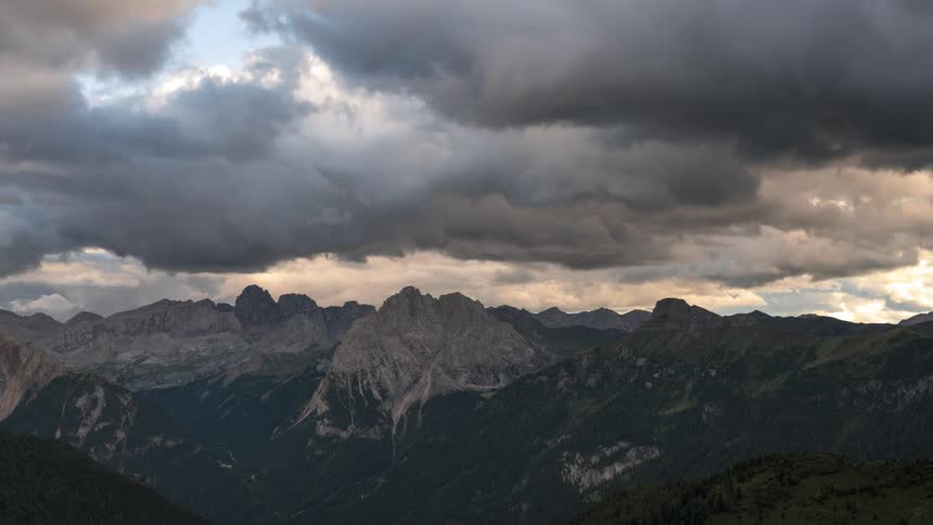 Heavy clouds flow over foggy mountainous terrain partially covered in forest