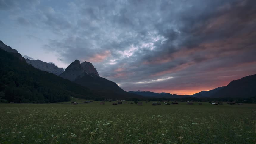 Clouds move across the sky over a rural town as the sun sets over the nearby mountains