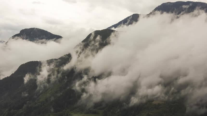 Some white clouds passing quickly over a mountain with forests of trees
