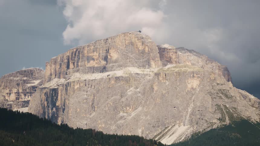 A large stone mountain with its surface illuminated by sunlight and many white clouds passing overhead