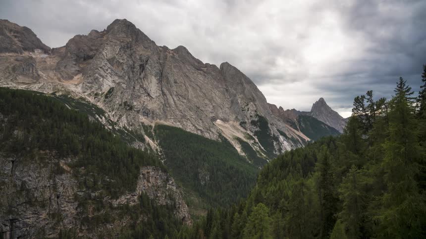 A landscape of a valley between mountains with several trees and white clouds passing in the sky