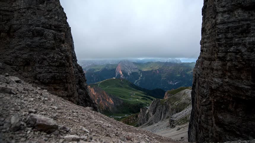 View between two large rock formations revealing a valley and distant mountains under a cloudy dusk sky