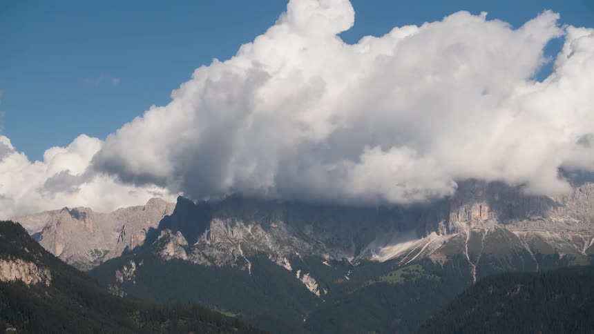 Some dense white clouds passing over the peak of a mountain range