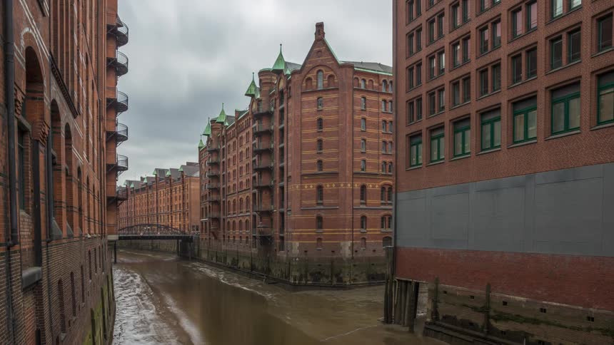 Narrow water canal flanked by red brick buildings with traditional architecture under a cloudy sky