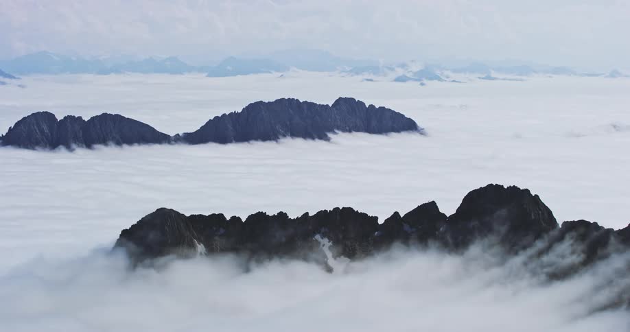 Series of dark mountain peaks emerging from a sea of white clouds