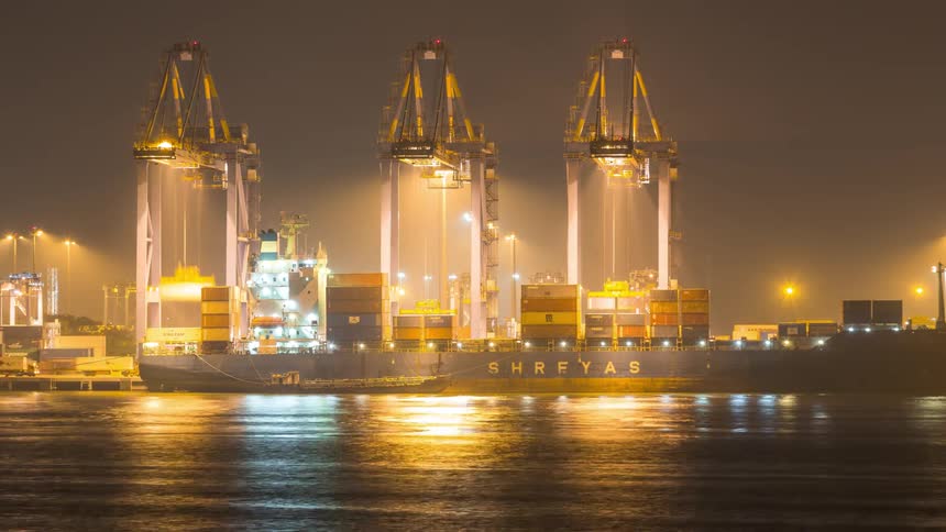 Night cargo ship docked in a port with several illuminated container cranes