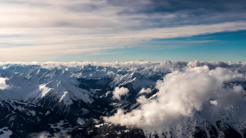 Landscape of snowy mountain ranges and clouds passing by on a blue sky morning