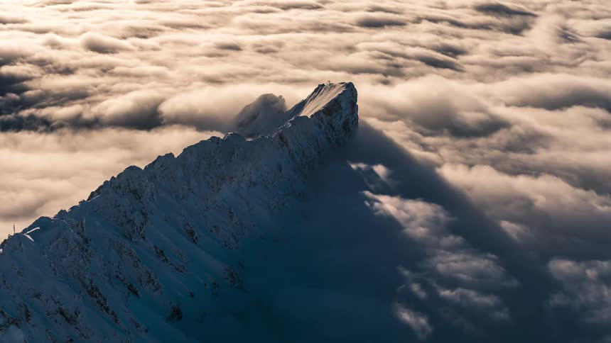The peak of a snowy mountain with a sea of clouds passing beneath