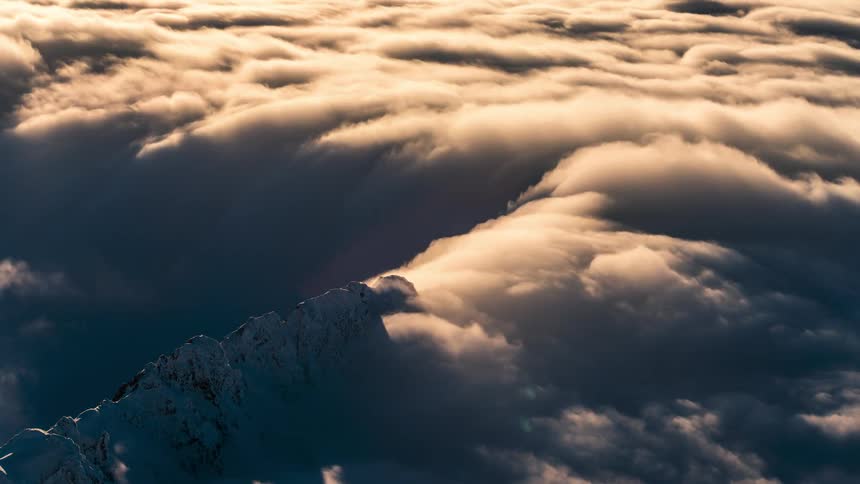 Aerial panorama of a mountain peak covered in snow with clouds passing by
