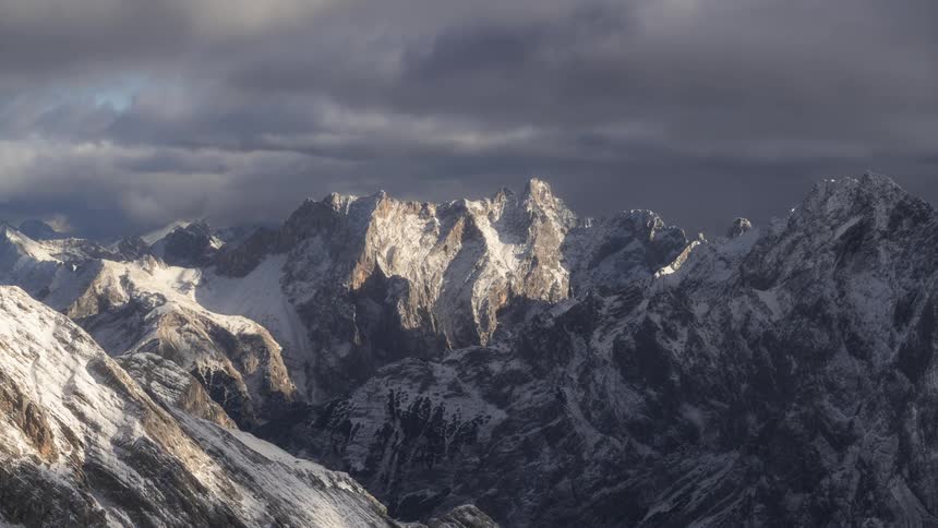 Flowing dark clouds cast shadows across snowy mountainous terrain