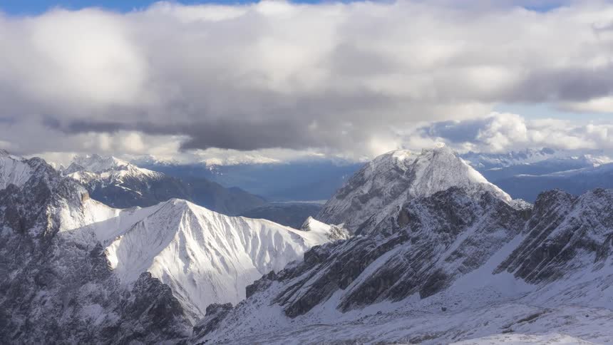 A mountain range with snowcapped mountains and white clouds passing quickly in the sky