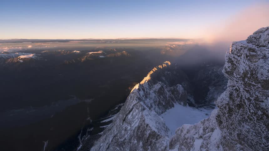 Aerial view of snow covered mountains during sunrise with clouds passing by