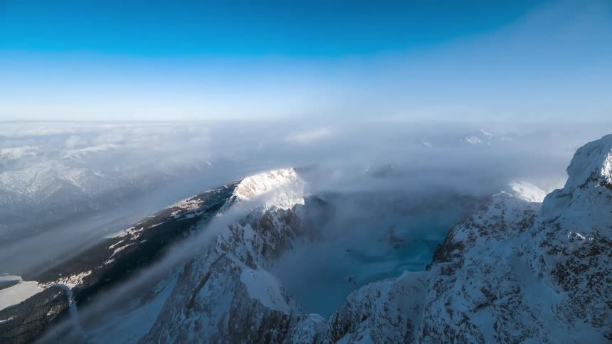 Time lapse of clouds rolling over snow covered steep mountain peaks under a blue sky