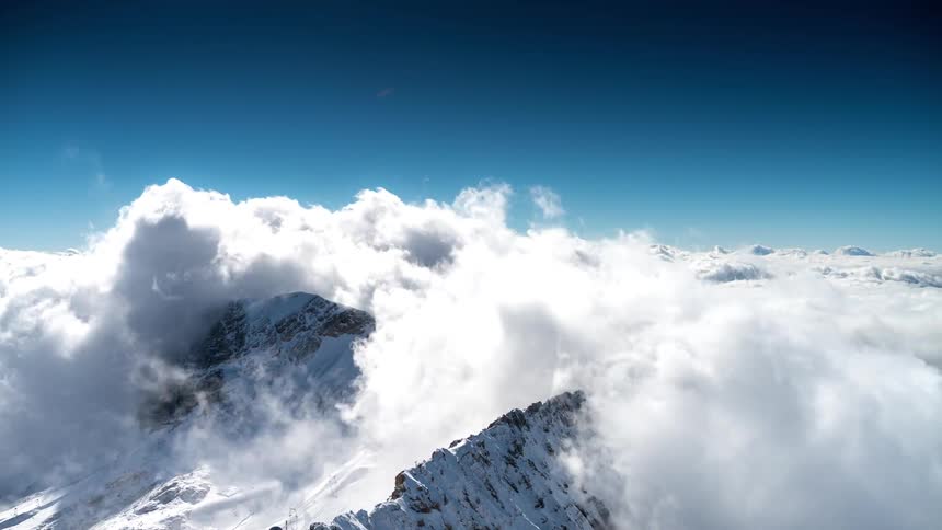 White clouds passing over the tops of icecovered mountains and above there is a clear blue sky