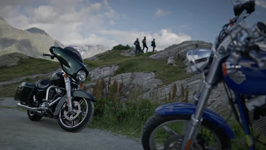 Three motorcyclists stand on an elevated area near their bikes parked on a road