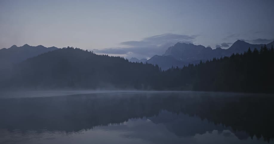 Fog moving across the rippling lake surface which reflects the surrounding mountains and trees