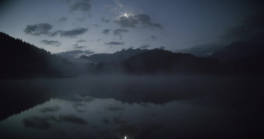 A lake reflecting mountains that are all around and the bright moon that is in the sky