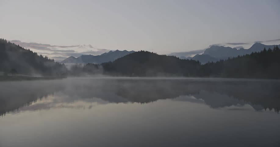 A misty lake reflecting the silhouette of mountains and trees