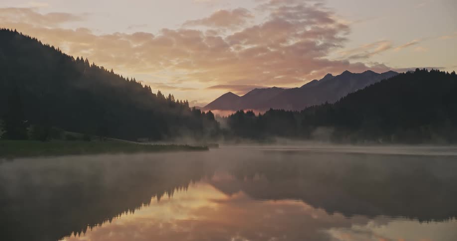 A lake reflects the nearby forests and mountains