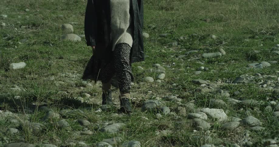 Legs of a person walking in an openair environment with rocks and grass around them