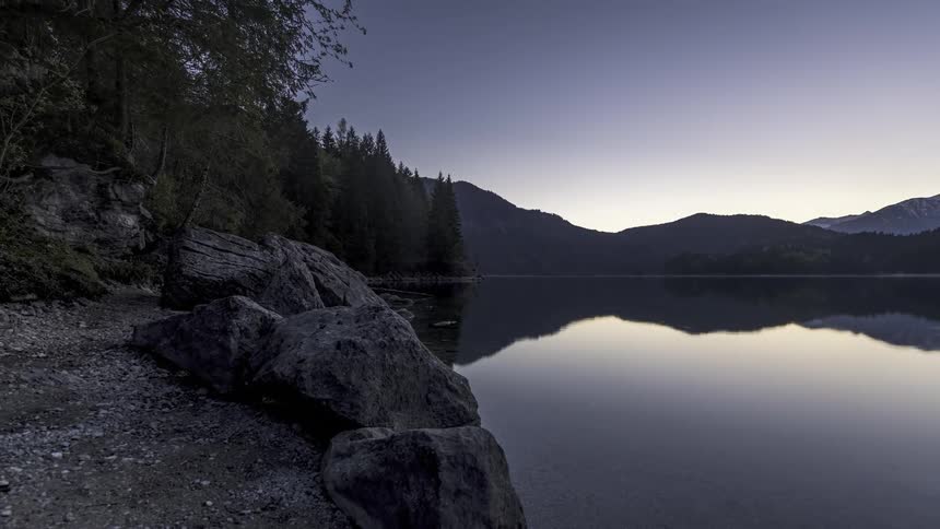 A large ripple moves across a lake near a shore and mountains