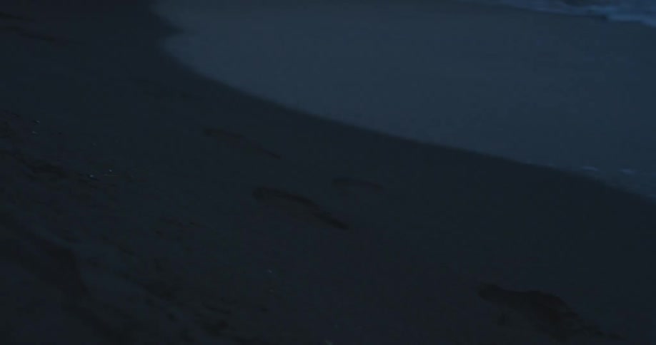 Waves wash up on a beach next to several footprints
