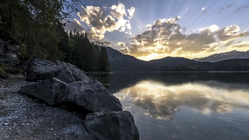 Time lapse of clouds rolling over a tranquil lakeside scene at sunset