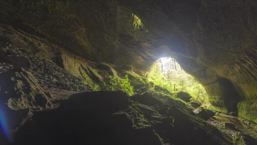 Sun shines through cave mouth into large sloping cavern